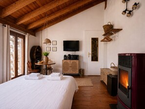 A cozy bedroom with a bed, a television, a fireplace, and a wooden ceiling.