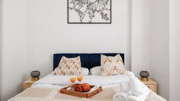 A neatly made bed with a tray of croissants and orange juice, a world map on the wall, and a blue headboard.