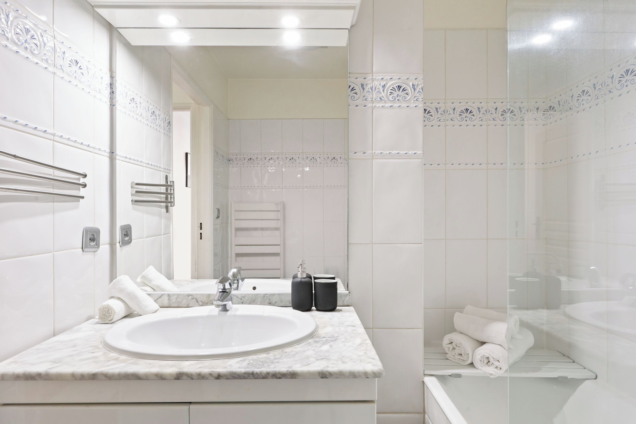 A modern bathroom with a marble sink, towel rack, and glass shower enclosure.
