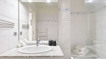 A modern bathroom with a marble sink, towel rack, and glass shower enclosure.