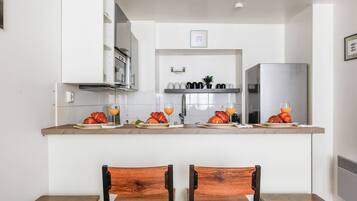 A kitchen with white cabinets, a stainless steel refrigerator, and a breakfast setup with croissants and orange juice.