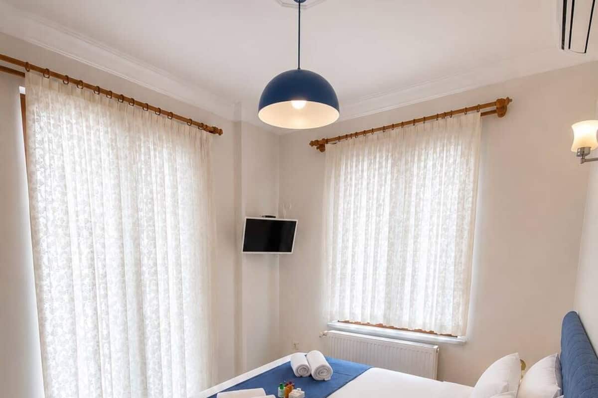 Quarto de hotel com cama, televisão, mesa de cabeceira e luminária.