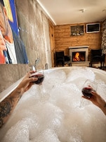 Una habitación con chimenea, televisor y una bañera llena de hielo, donde dos personas sostienen copas de vino.