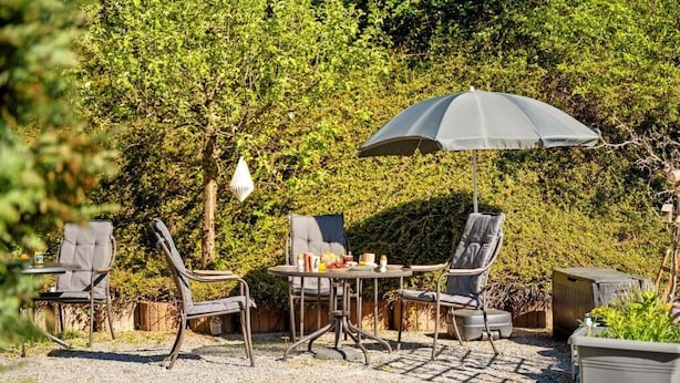 An outdoor seating area with metal chairs and a table, surrounded by greenery. - Harzträume Apartments Wernigerode (Wernigerode)