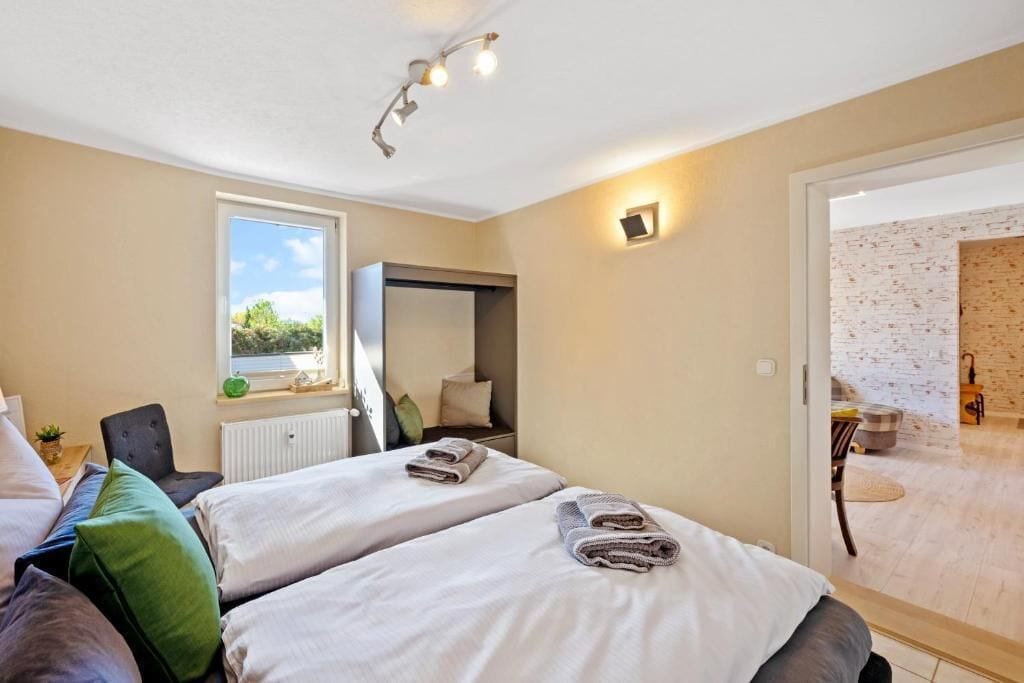 A bedroom with two beds, a window, a radiator, a mirror, and a door leading to a bathroom.