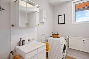 Ein Badezimmer mit Waschbecken, Spiegel, Handtuchhalter und einer Waschmaschine.