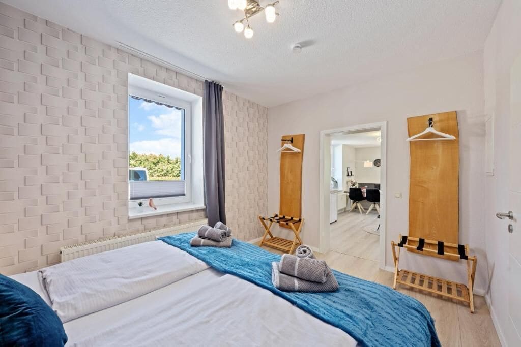 A hotel room with two beds, a window with a view, a wooden drying rack, and a mirror.