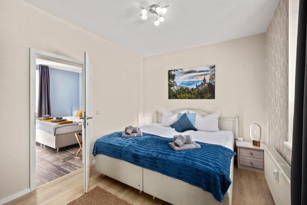 A bedroom with a bed, a nightstand, a mirror, a picture on the wall, and a door leading to another room.