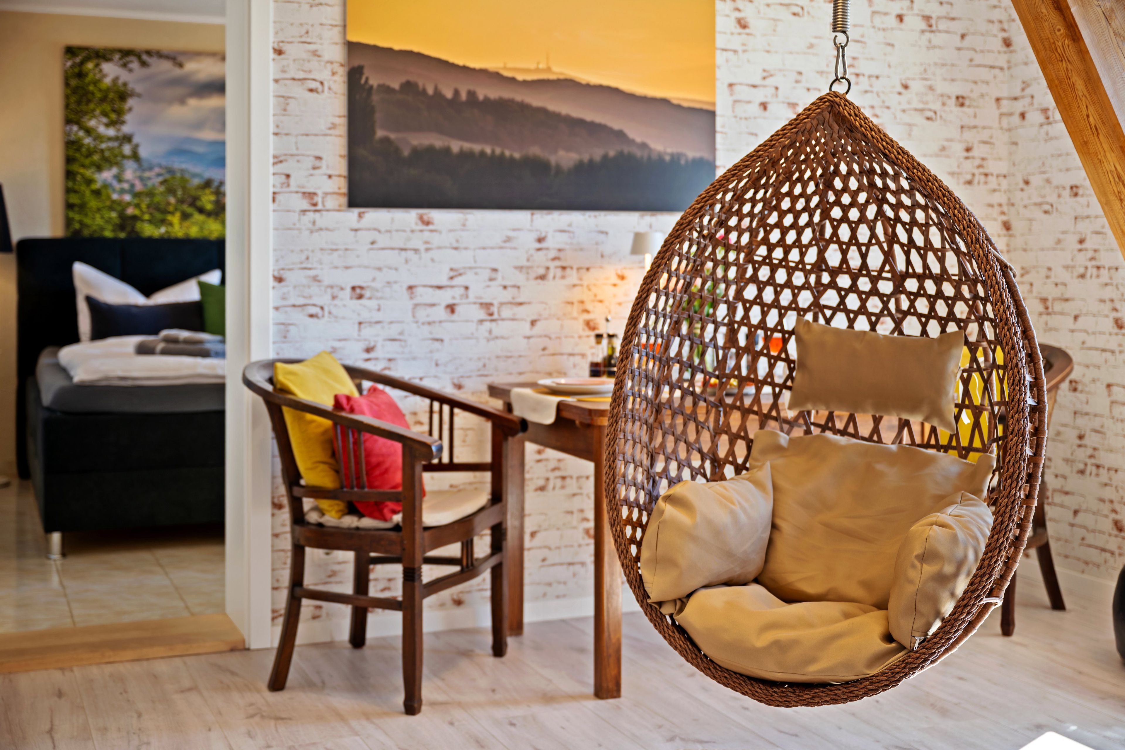 Um quarto aconchegante com uma cadeira suspensa, uma mesa de jantar de madeira e uma cama com almofadas.