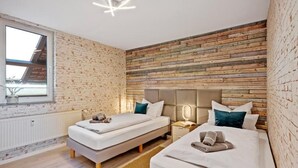 A modern bedroom with two beds, a brick-patterned wall, a skylight, and a nightstand with a lamp. - Harzträume Apartments Wernigerode (Wernigerode)