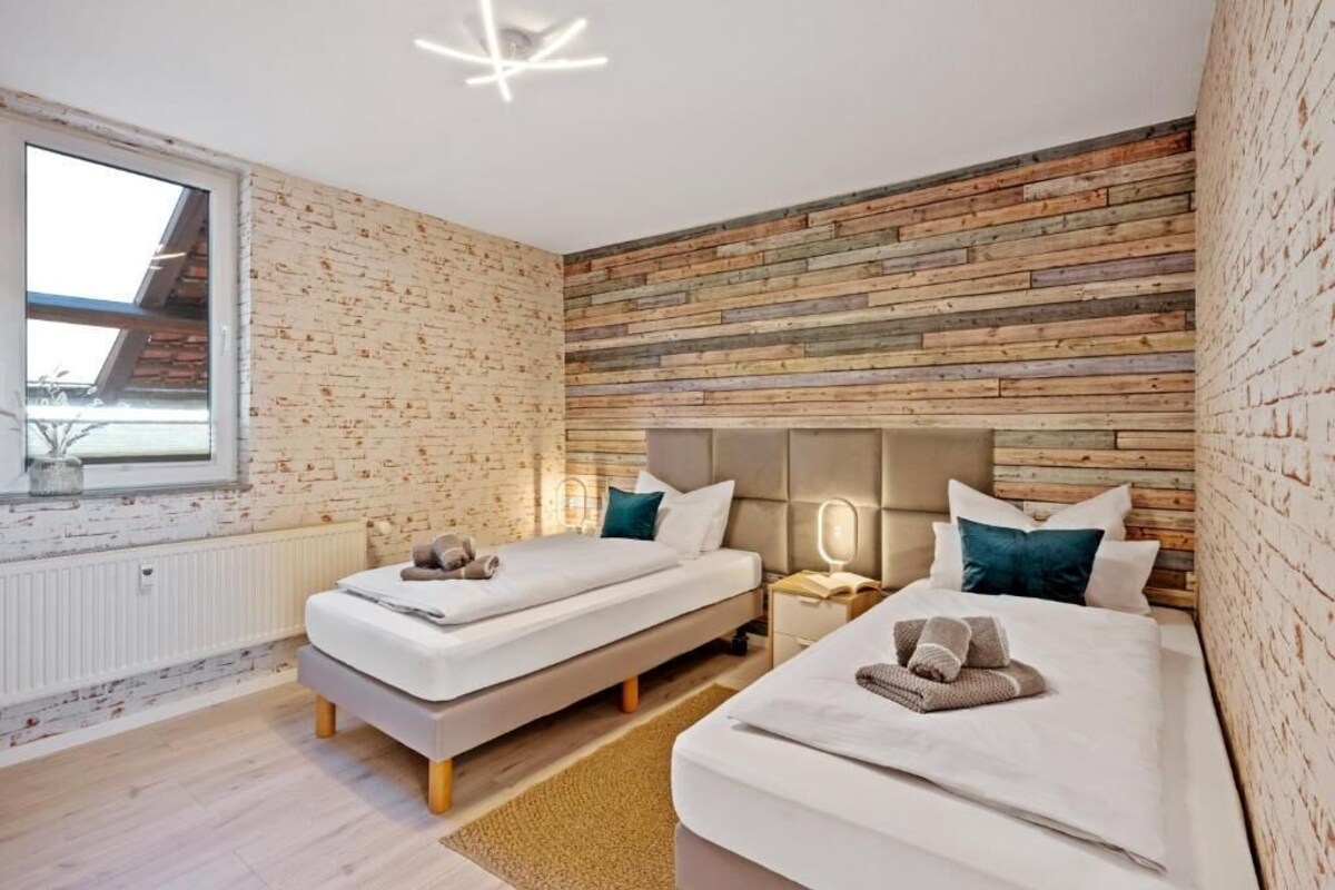 Ein modernes Schlafzimmer mit zwei Betten, einer Ziegelwand, einem Oberlicht und einem Nachttisch mit Lampe.