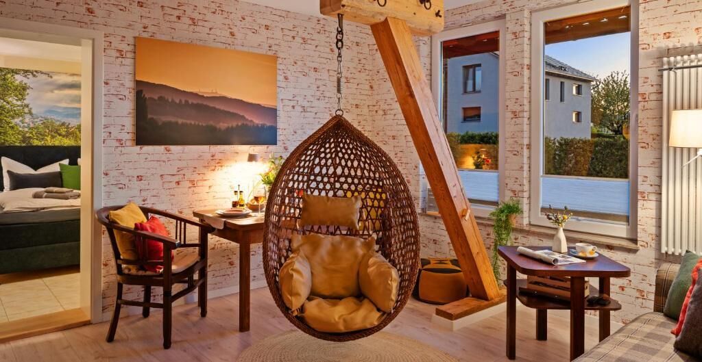 Une pièce avec un fauteuil suspendu, une table avec une lampe, un canapé et un tableau au mur.