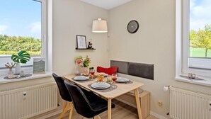 A dining area with a table set for two, a clock on the wall, and a window with a view of greenery. - Harzträume Apartments Wernigerode (Wernigerode)