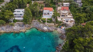 Eine Luftaufnahme einer Küstenregion mit Häusern, einer felsigen Uferlinie und klarem türkisblauem Wasser.