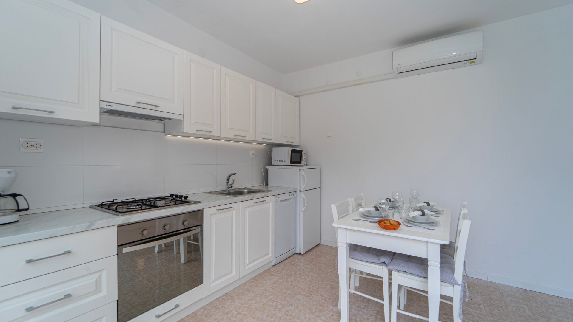 A modern kitchen with white cabinets, a gas stove, a microwave, and a dining area with a table set for two.