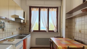 Una cucina con una finestra, un tavolo con tovaglia a quadretti e una lavatrice.