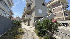 Un edificio residenziale a più piani con balconi, una scala centrale e un vialetto lastricato.