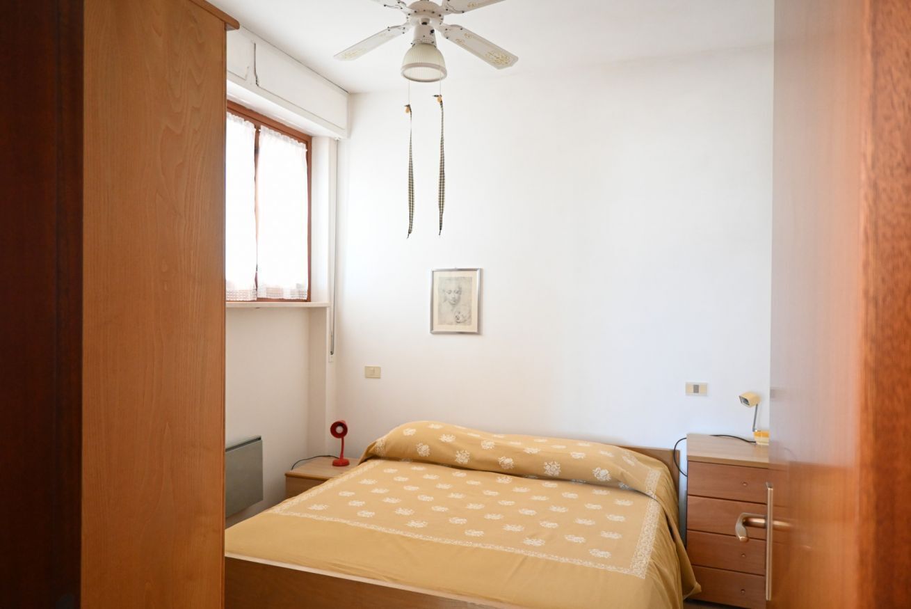 Un dormitorio con cama, cómoda de madera, ventilador de techo, ventana y un cuadro colgado en la pared.