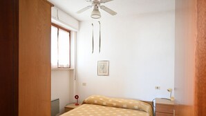 Una camera da letto con un letto, una cassettiera in legno, una ventola a soffitto, una finestra e un quadro appeso al muro.