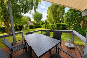 A covered outdoor deck with a table and chairs, surrounded by greenery and trees. - Wildgans 29 - Classic Scandinavian vacation home for up to 6 people (Mirow)