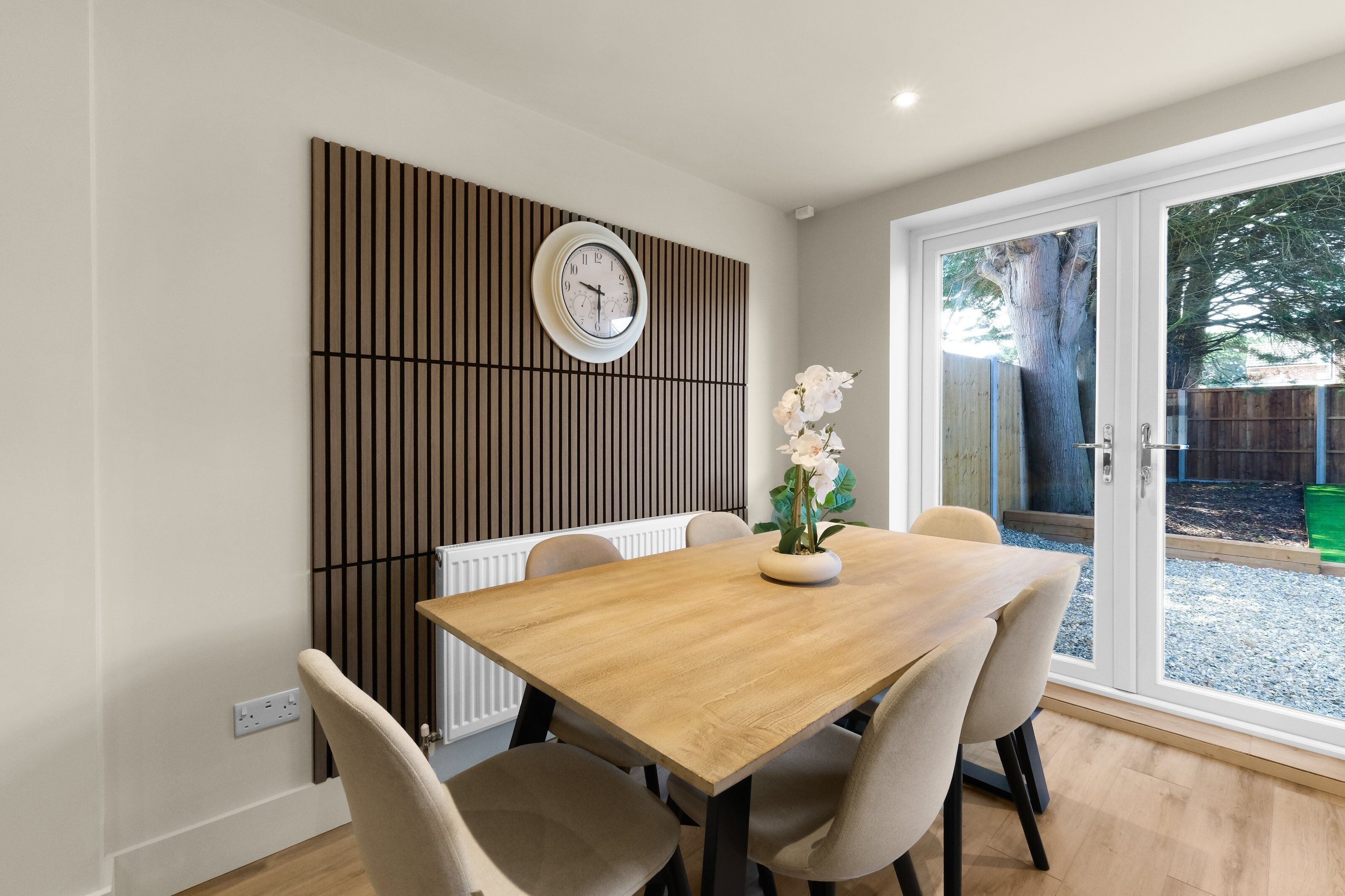 Un comedor con una mesa de madera, sillas, un reloj en la pared y vistas a través de un ventanal.