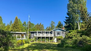 A two-story house with a porch, surrounded by lush greenery and tall trees. - Cozy home in Motala with sauna (Motala)