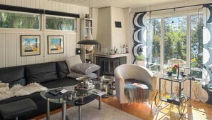 A living room with a black leather sofa, a glass coffee table, a white armchair, and a fireplace. - Cozy home in Motala with sauna (Motala)