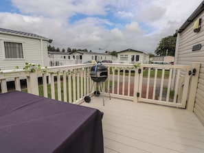 Une terrasse avec un barbecue, une table et une clôture blanche.
