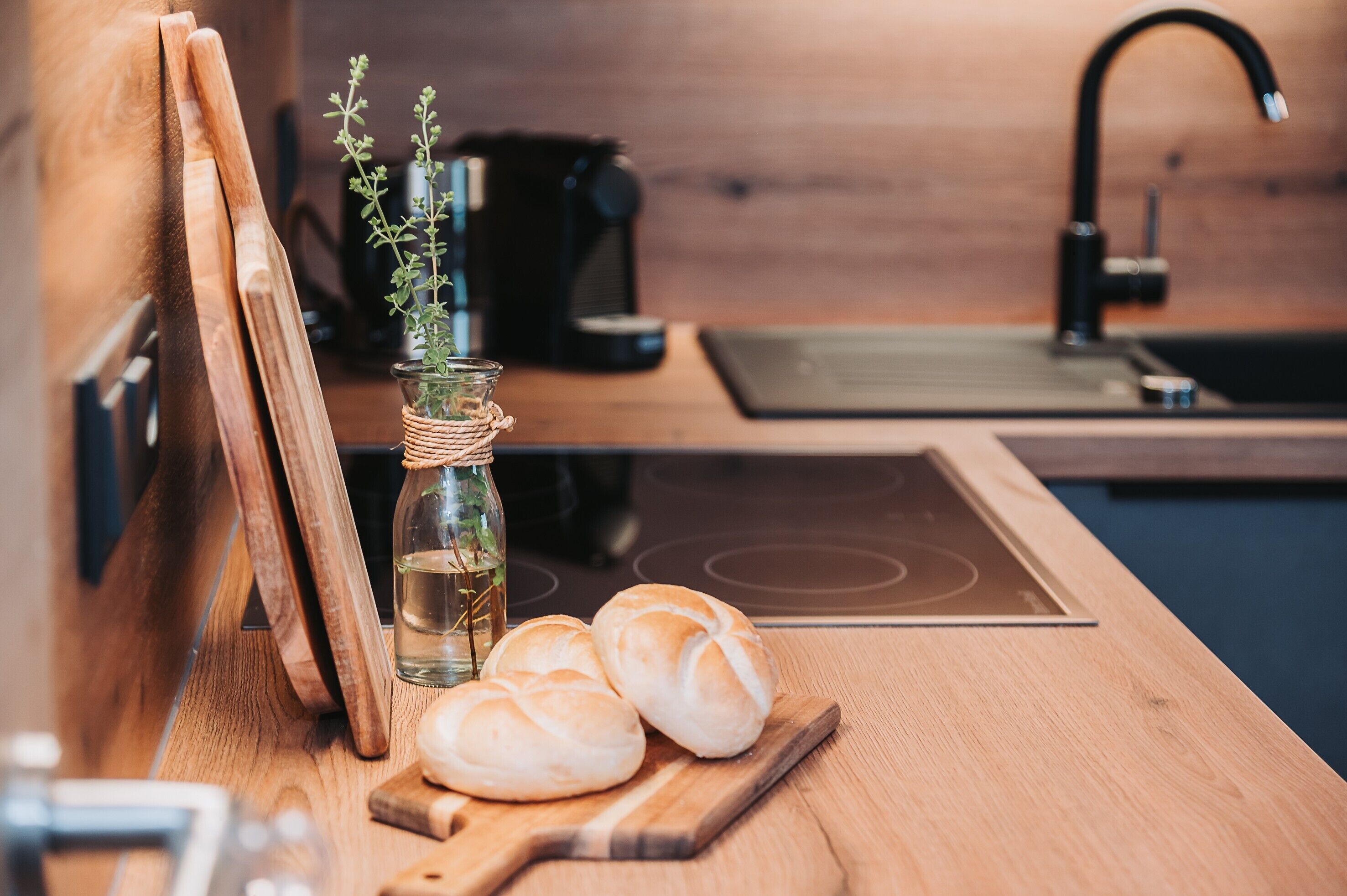 Un plan de travail en bois sur lequel on aperçoit une bouteille en verre, une plante et deux pains.