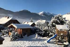 Ein schneebedecktes Dorf mit Holzhäusern, einem Spielplatz und einem Berg im Hintergrund.