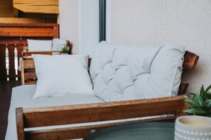 Ein hölzernes Bett mit weißer Bettwäsche, ein Holz-Kopfteil und ein kleiner Topfpflanze seitlich.