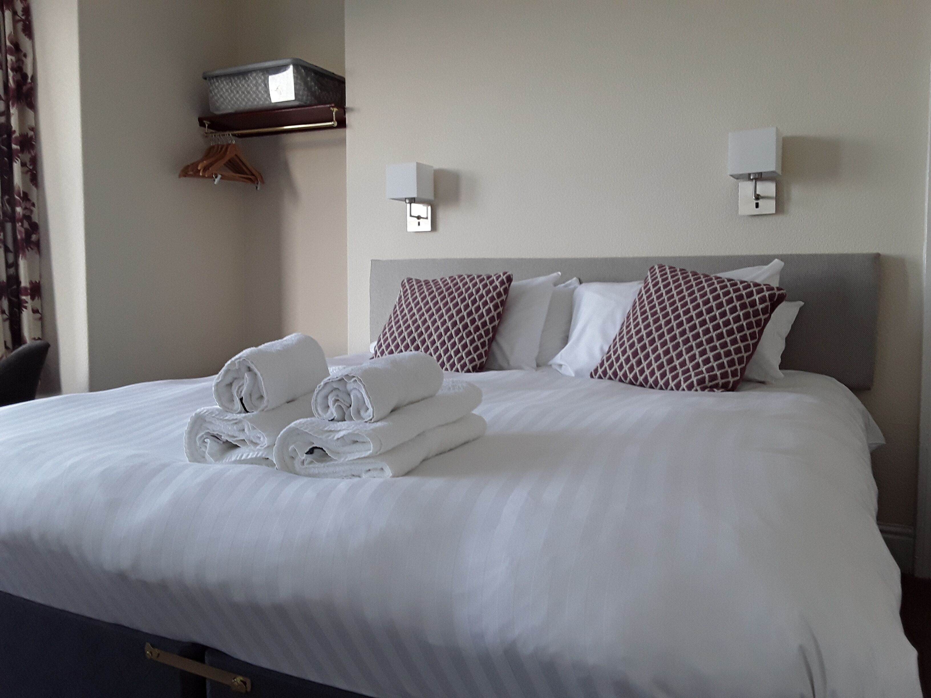 A neatly made bed with rolled towels, a headboard, and two wall-mounted light fixtures.