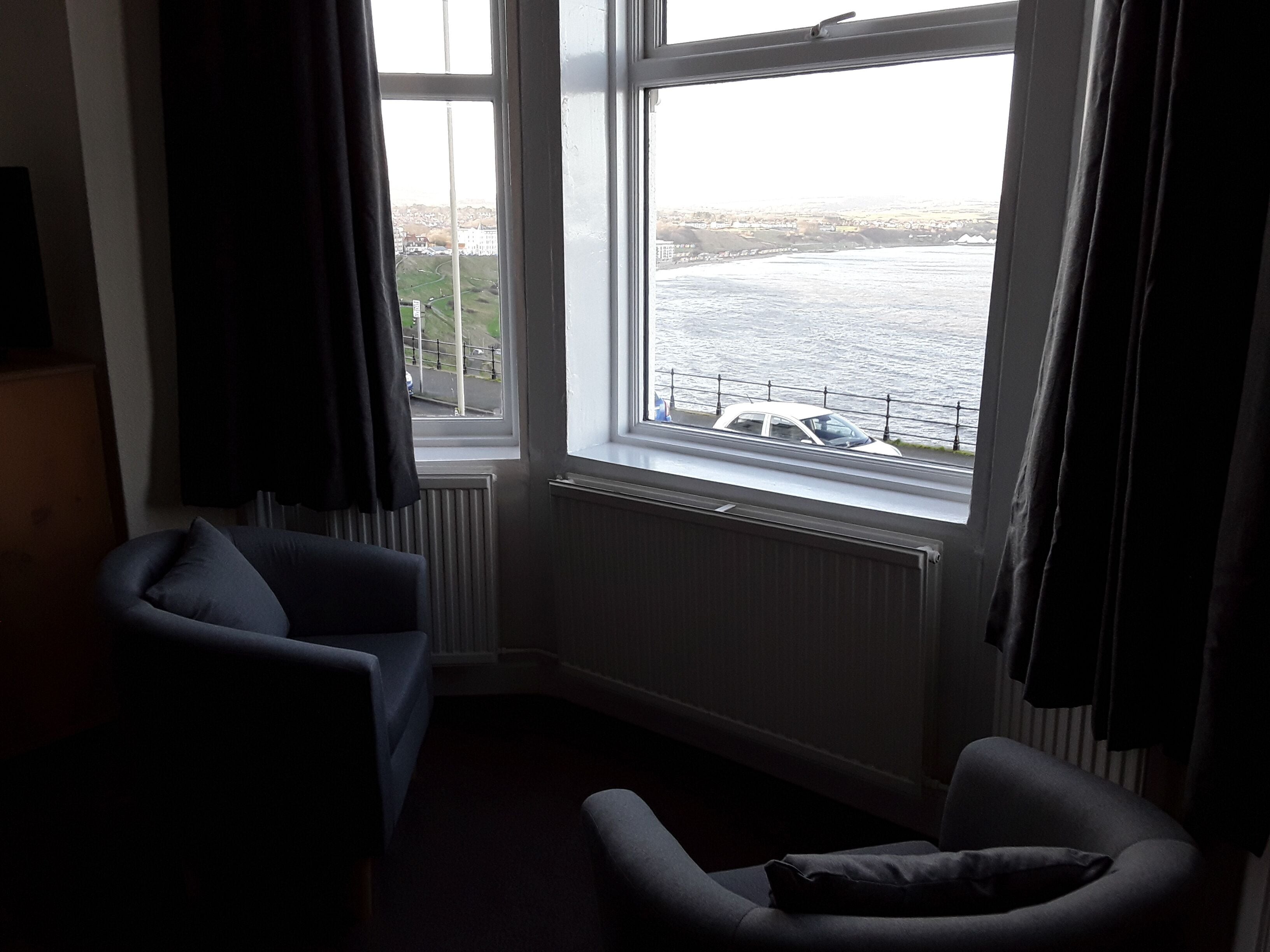 Habitación con ventana grande con vistas a un cuerpo de agua, un radiador y dos sillones.