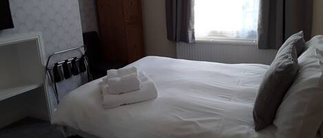 A hotel room with a bed, a wooden wardrobe, a radiator, and a window with curtains.