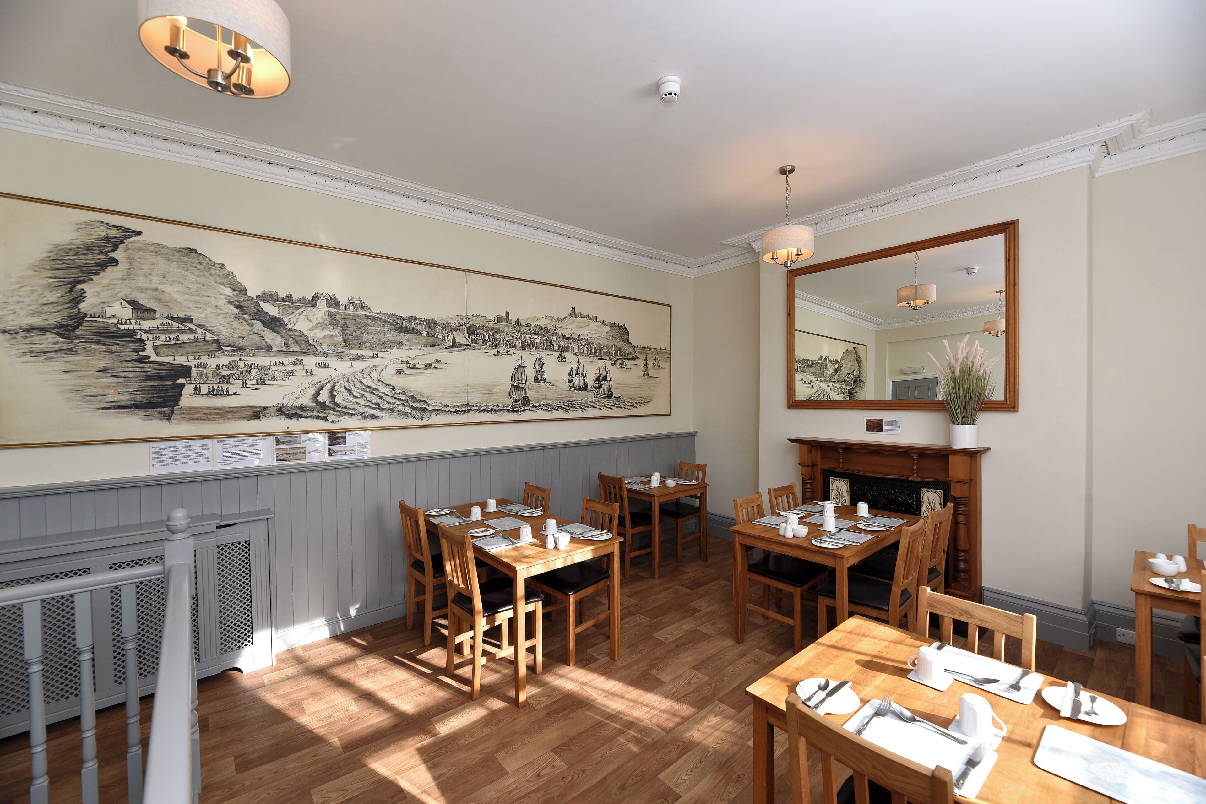 Un comedor con mesas y sillas de madera, un mural grande en blanco y negro en la pared y una chimenea.