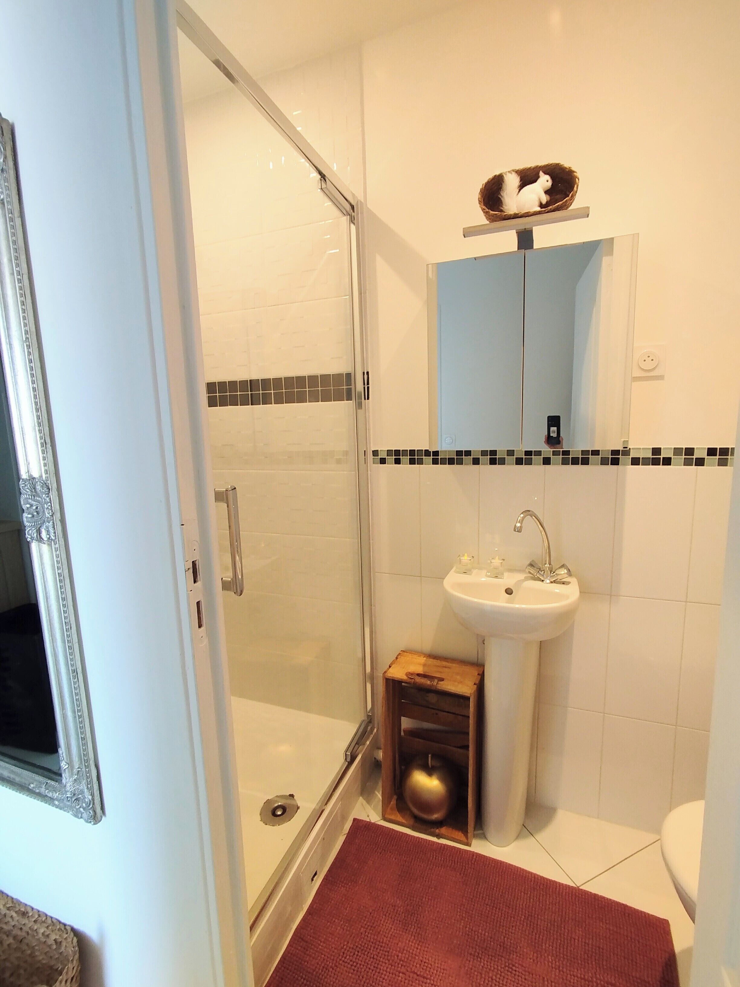 Un baño con cabina de ducha de vidrio, un lavamanos con espejo y un taburete de madera.