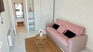A living room with a pink sofa, a round wooden coffee table, a white vase with flowers, and a white tiled floor.