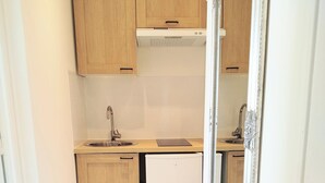 A compact kitchen with wooden cabinets, a built-in dishwasher, and a large mirror.