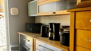 A kitchen with wooden cabinets, a microwave, a coffee maker, and a trash bin. - Parenthese à Montady - 6personnes - PMR - Terrasses (Montady)