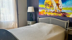 A bedroom with a bed, a ceiling fan, a painting, a lamp, and a window with curtains. - Parenthese à Montady - 6personnes - PMR - Terrasses (Montady)