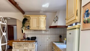A kitchen with a central island, tiled floor, wooden cabinets, and a refrigerator. - IN THE SHADE OF THE OLIVE TREE IN GRAU D'AGDE (Agde)