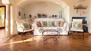 Un salon avec un canapé blanc, deux fauteuils, une table basse et des objets décoratifs accrochés aux murs.