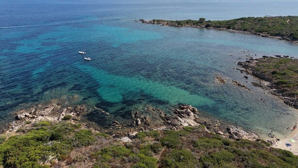 Un paysage côtier caractérisé par des eaux limpides, des rivages rocheux et des montagnes à l’horizon.