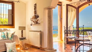 Une chambre avec vue sur la mer, un radiateur, une table avec des chaises et un canapé agrémenté de coussins décoratifs.