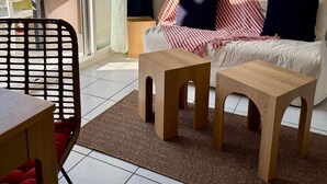 Un saló modern amb un sofà, dues taules laterals de fusta, una cadira de vímet, una taula de vidre i una porta corredissa de vidre que dona a una zona exterior.