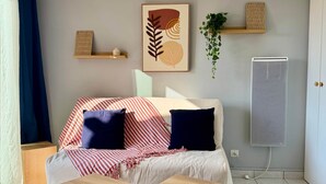 Habitació amb un llit, dues taules laterals de fusta, un radiador i una prestatgeria penjada amb objectes decoratius.