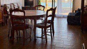 A dining area with a table and chairs, a television, and a view of a body of water through large windows. - THE TAMARISSIERE RETREAT (Agde)
