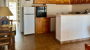 A kitchen with wooden cabinets, a refrigerator, an oven, and a dining area with a table and chairs. - THE TAMARISSIERE RETREAT (Agde)