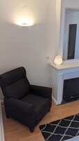Une pièce d’angle avec un fauteuil noir, une applique murale blanche et une cheminée dotée d’un manteau de cheminée blanc.
