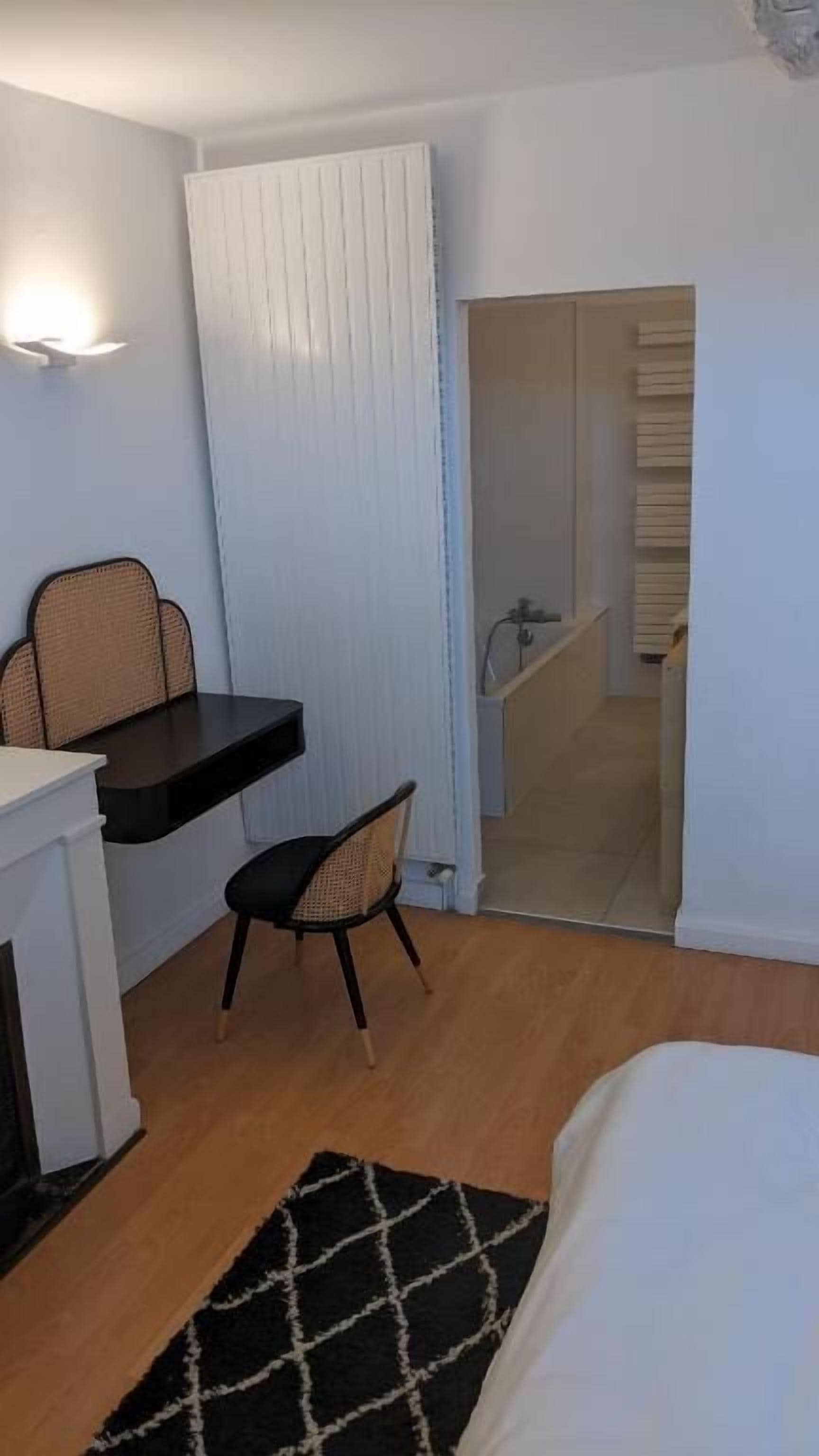 Une chambre à coucher avec un lit, un bureau avec une chaise, un petit tapis et une salle de bain visible à travers une porte ouverte.